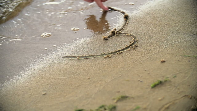 Female hand drawing heart in seashore sand  