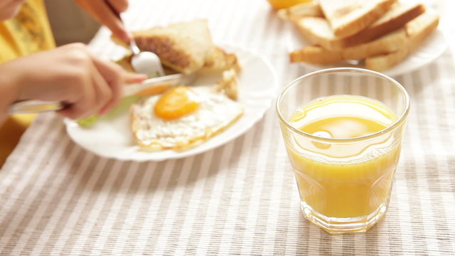 Hungry little pupil cuts his fried eggs during the breakfast