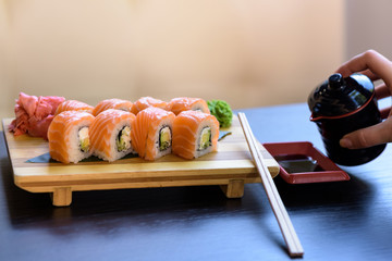Philadelphia sushi rolls with chopsticks, wasabi and ginger on a wooden food plate