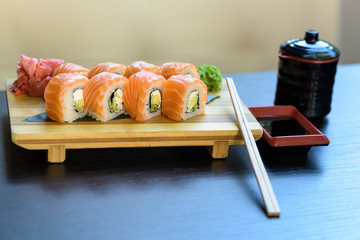 Philadelphia sushi roll with chopsticks, wasabi and ginger on a wooden food plate