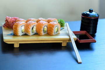Philadelphia sushi roll with chopsticks, wasabi and ginger on a wooden food plate