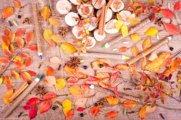 Colorful autumn leaves, spices, cinnamon, cloves, cardamom, anise and pensils lying on wooden background. Fall and thanksgiving setting. Autumn composition.
