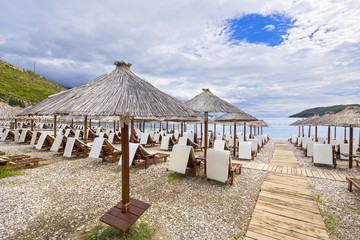 Thatched umbrellas and beach chairs on the beach. Budva, Montenegro