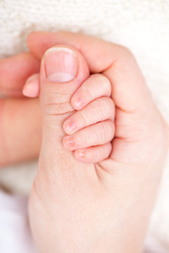 Newborn baby holding mother's thumb