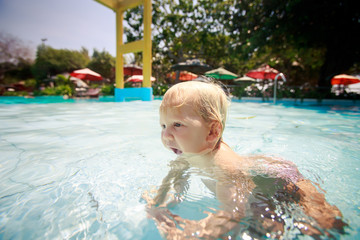 small blonde girl swim transparent water of pool