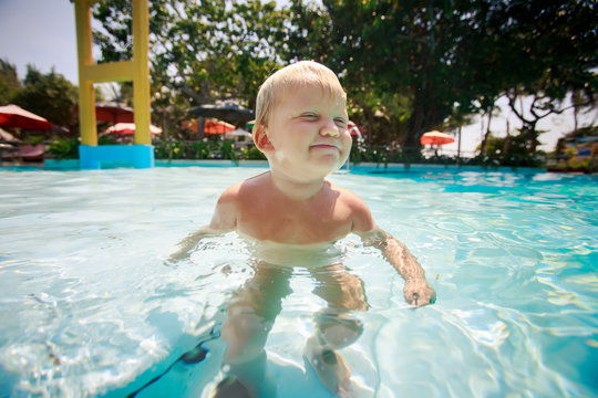 small blonde girl swims with joy in water of pool