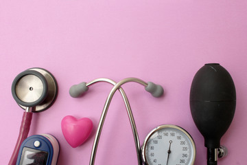 Medicine concept - stethoscope, blood pressure equipment, heart and pulse oximetere on pink background
