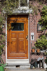 Brown wooden door of a brick home with a garden. Jackboots and watering can next to the door
