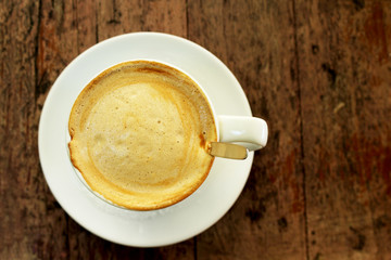 Cup of coffee with foam in a white cup on wooden background