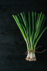 Bunch of young green onions on a black wooden background top view