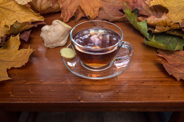 Hot tea with ginger framed by leaves on wooden table