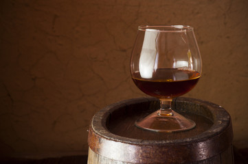glass of brandy in the cellar with old barrels stacked