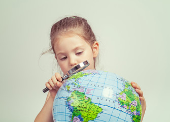 beautiful cute little girl looking through magnifying glass at globe