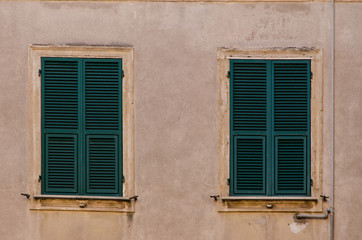 Fototapeta na wymiar two old windows with wooden shutters on a weathered stone exterior building wall