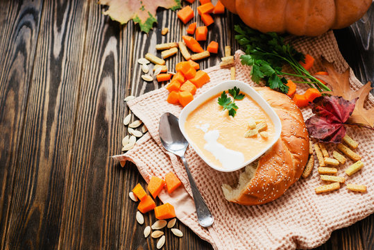 mashed pumpkin soup with herbs , cream , crackers and bread with sesame seeds on a wooden background
