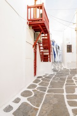 A very traditional alley view of the architecture in Chora, on the greek island Mykonos, Greece. A red door, balcony, fence and windows of a whitewashed house.