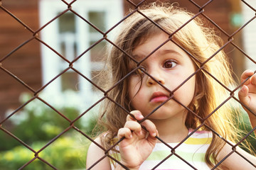 Toned portrait of Sad little girl looks through wire fence