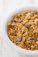 granola with chocolate on white bowl on white wooden background