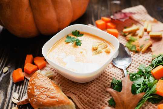 mashed pumpkin soup in a clay plate with herbs , cream , crackers and bread with sesame seeds on a wooden background