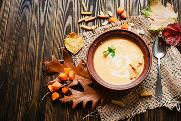 mashed pumpkin soup in a clay plate with herbs , cream , crackers and bread with sesame seeds on a wooden background