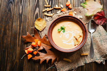 mashed pumpkin soup in a clay plate with herbs , cream , crackers and bread with sesame seeds on a wooden background