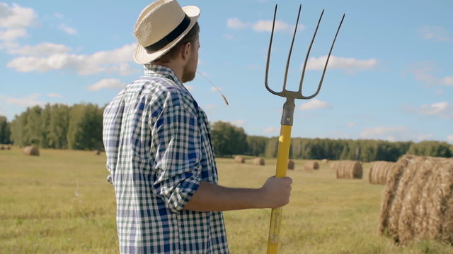 Farmer with pitchfork looking at hay bales in field 
