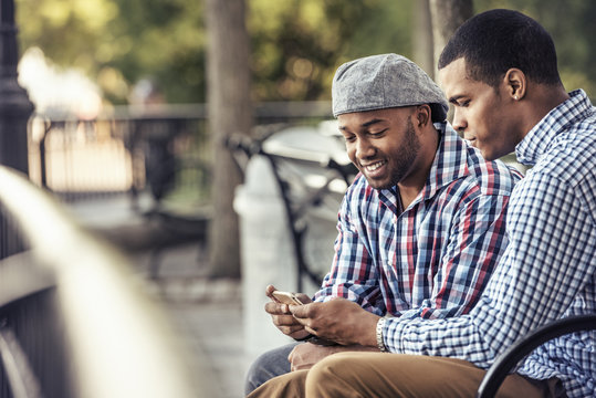 Two men sitting in a park, looking at a smart phone