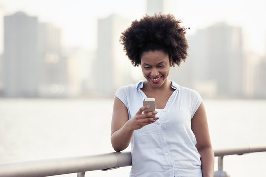 A woman leaning on a waterfront rail checking her cell phone