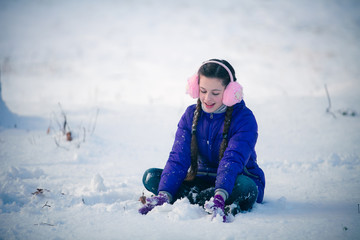 Fototapeta na wymiar Pretty young girl is kneeling in the snow
