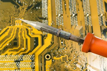 Soldering iron with red handle over a printed circuit board