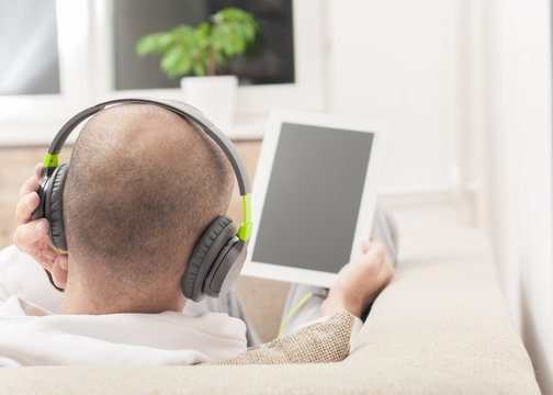 Man using digital tablet computer at home wearing headphones 