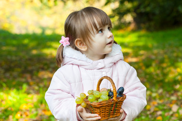     Girl with pigtails holding a wicker basket with grapes and apples 