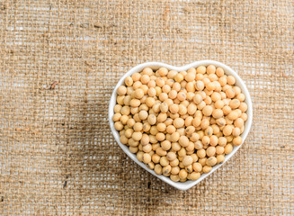 soybeans in heart ceramic bowl on sackcloth background..