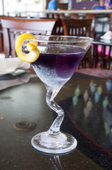 purple cocktail drink in a bar with a lemon twist 