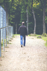 A man is walking the path next to a high metal fence. Image has a vintage effect applied.