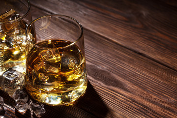Glasses of whiskey with ice on wood
