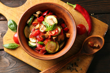 Tasty vegetarian ratatouille made of eggplants, squash, tomatoes in bowl on wooden table background