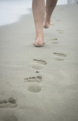 Feet of man and footprints on sand of beach