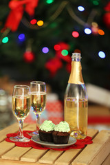Naklejka na ściany i meble Delicious cupcakes and champagne on table, on Christmas tree background