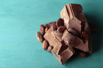 Milk chocolate pieces and cocoa beans on color wooden background