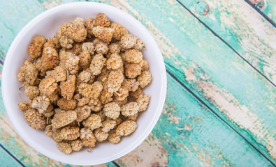 Dried white mulberry in white bowl over wooden background