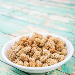 Dried white mulberry in white bowl over wooden background