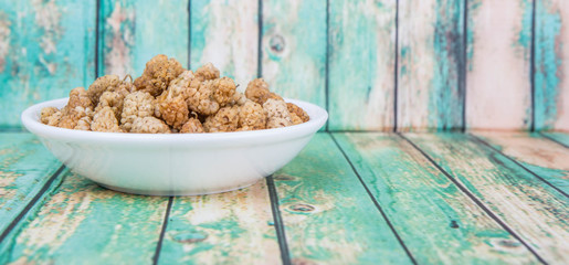 Dried white mulberry in white bowl over wooden background