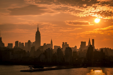 An orange sky sunrise behind a silhouette of Manhattan’s Skyline seen from the Hudson River