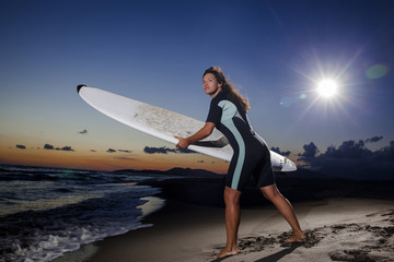 Young female surfer on beach in sunset