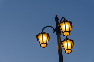 Fototapeta na wymiar vintage street lamp lantern glowing with wonderful warm light in front of a blue sky in the evening