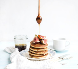 Pancake tower with fresh figs and honey on a rustic plate. White background