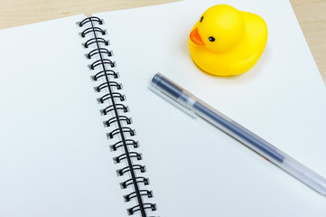 Pen and notebook and Rubber Duck on wooden desk