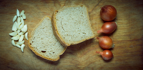 Onions garlic and slices of bread on a rustic wooden table.