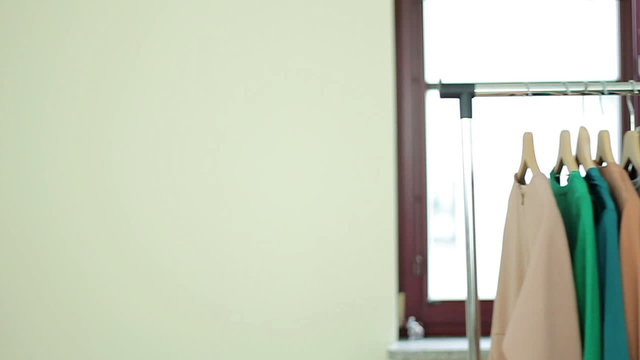 Young smiling woman pushing a movable rack of clothes, slow motion